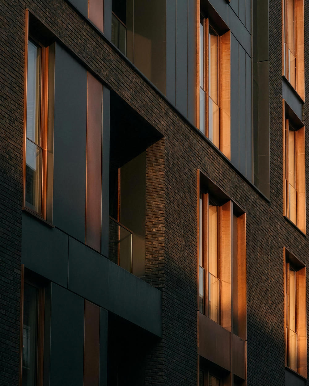 Donkere gevel van een hedendaags Amsterdams gebouw, koperkleurige kozijnen die avondlicht vangen